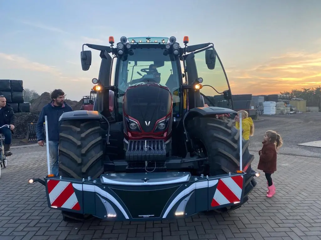 Box 50L without front linkage mounted on a tractor, with people standing around on a paved surface at sunset