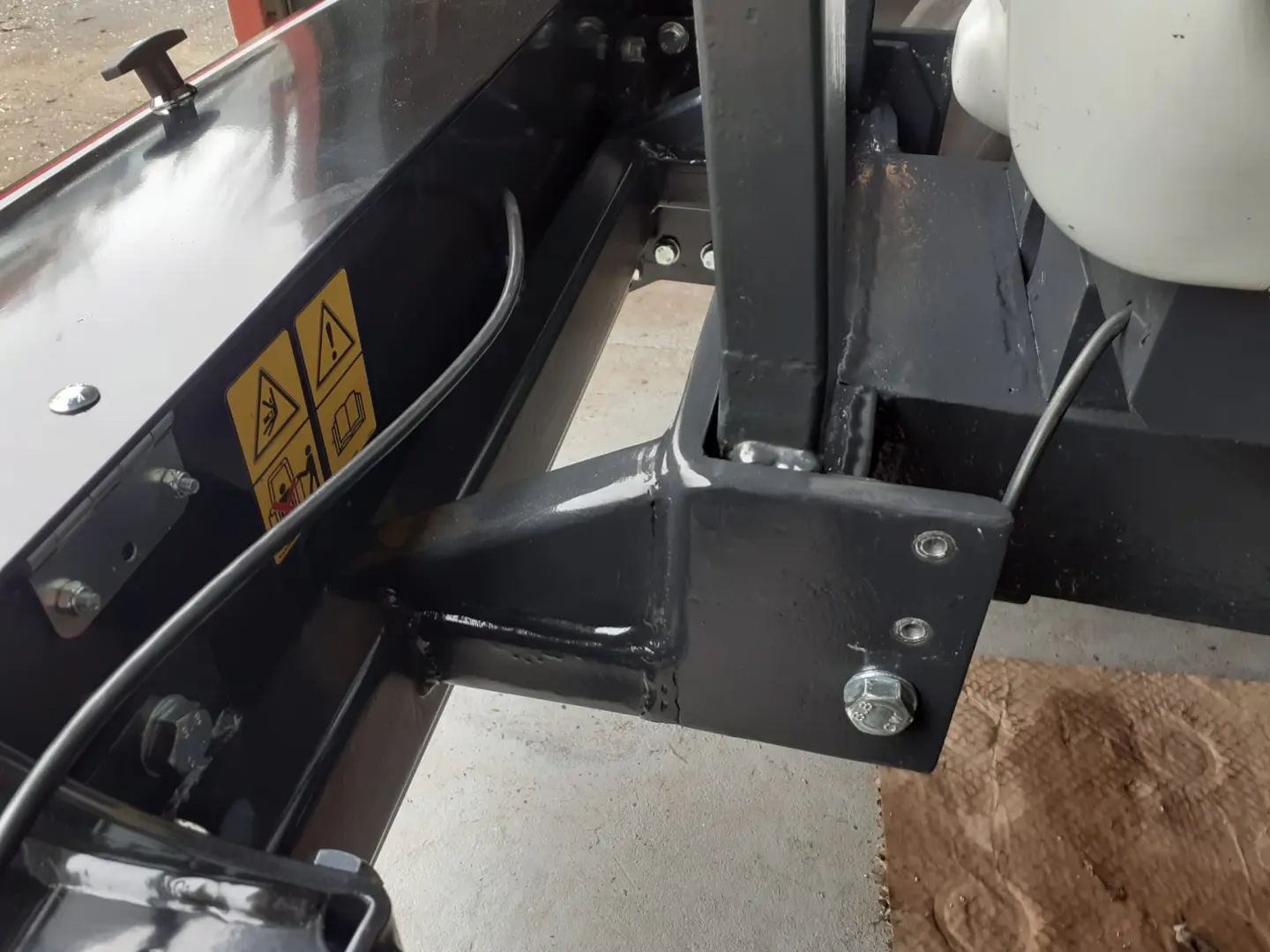 Close-up view of a Box 50L without front linkage attached to a tractor, showing mounting bolts and warning labels