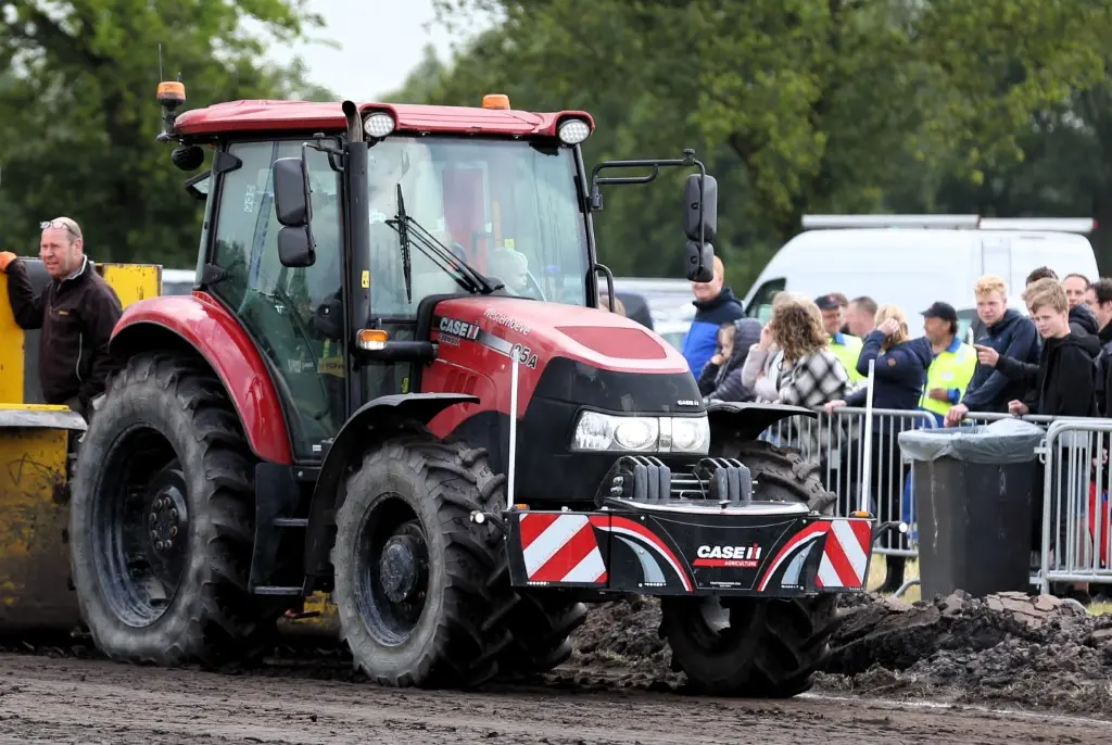 A tractor fitted with a Box 50L without front linkage weight bumper on muddy ground, with people watching nearby