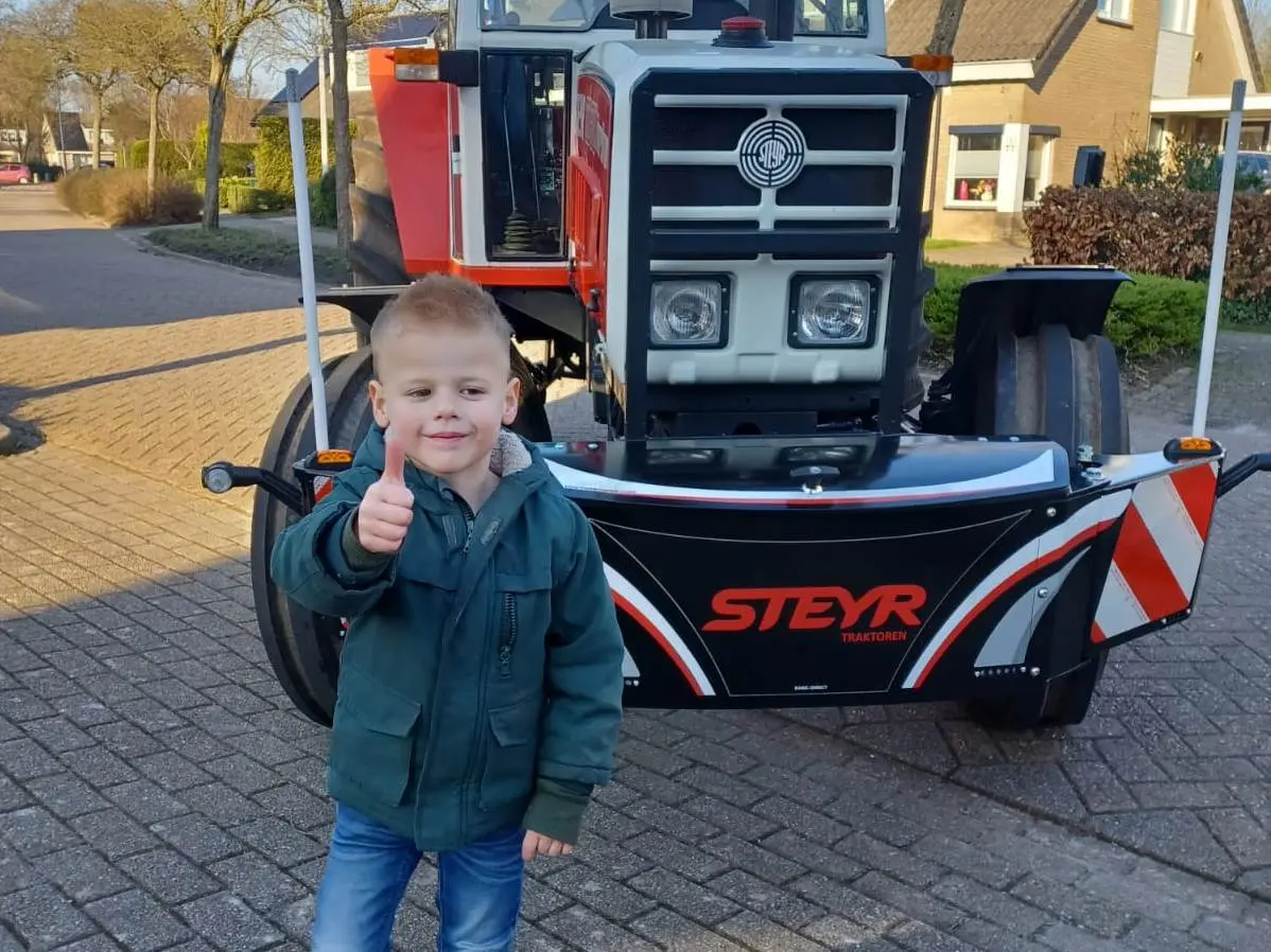 A young boy giving a thumbs-up stands in front of a tractor fitted with a Box 50L without front linkage front weight bumper.