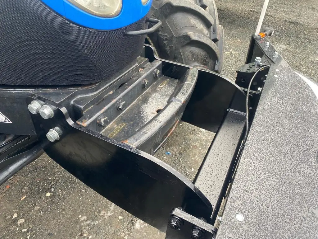 Black metal Box 50L without front linkage mounted on the front of a tractor above a wet gravel surface