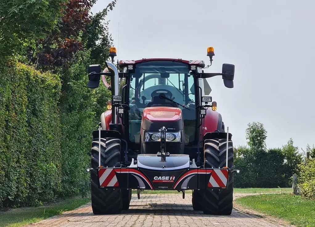 Red tractor with a front weight bumper featuring CASE IH branding and reflective safety markings on a paved path