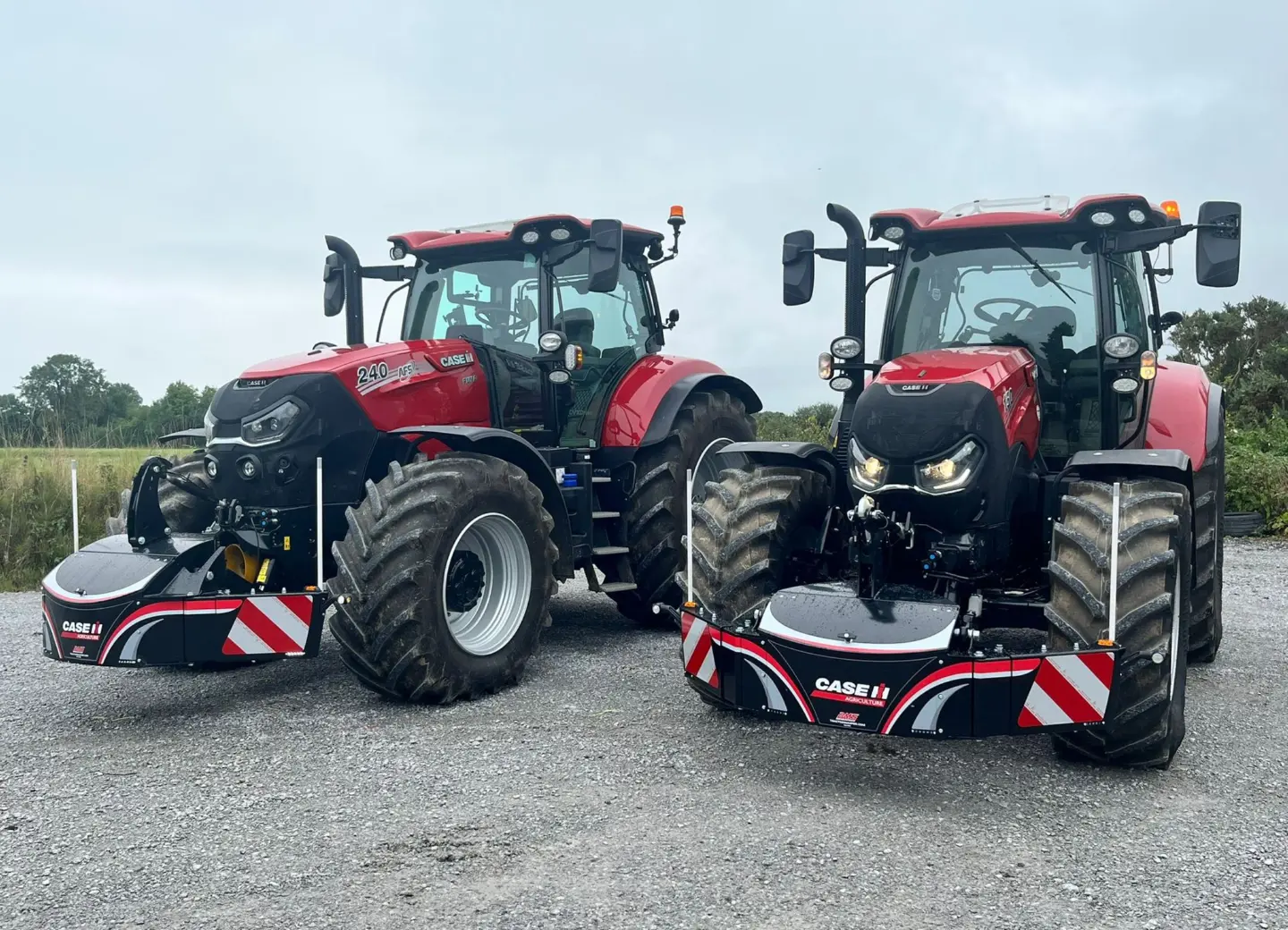 Two red tractors with large front weight bumpers featuring reflective stripes and Case IH branding on gravel