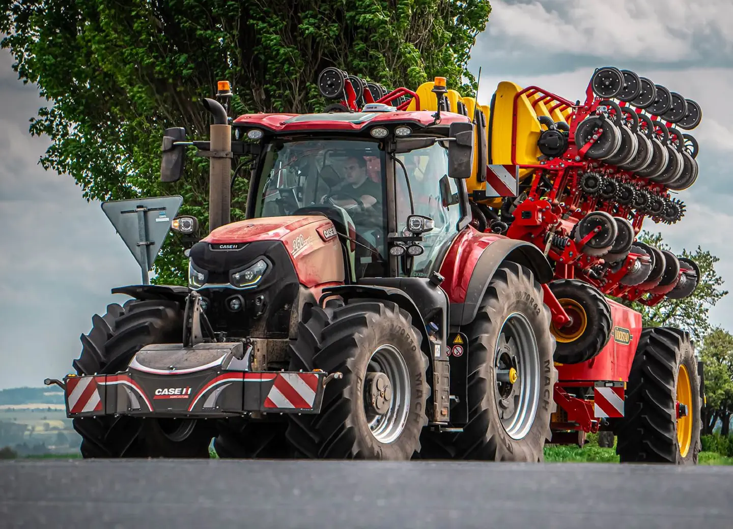 Red tractor with large front weight bumper and agricultural machinery attached on a rural road