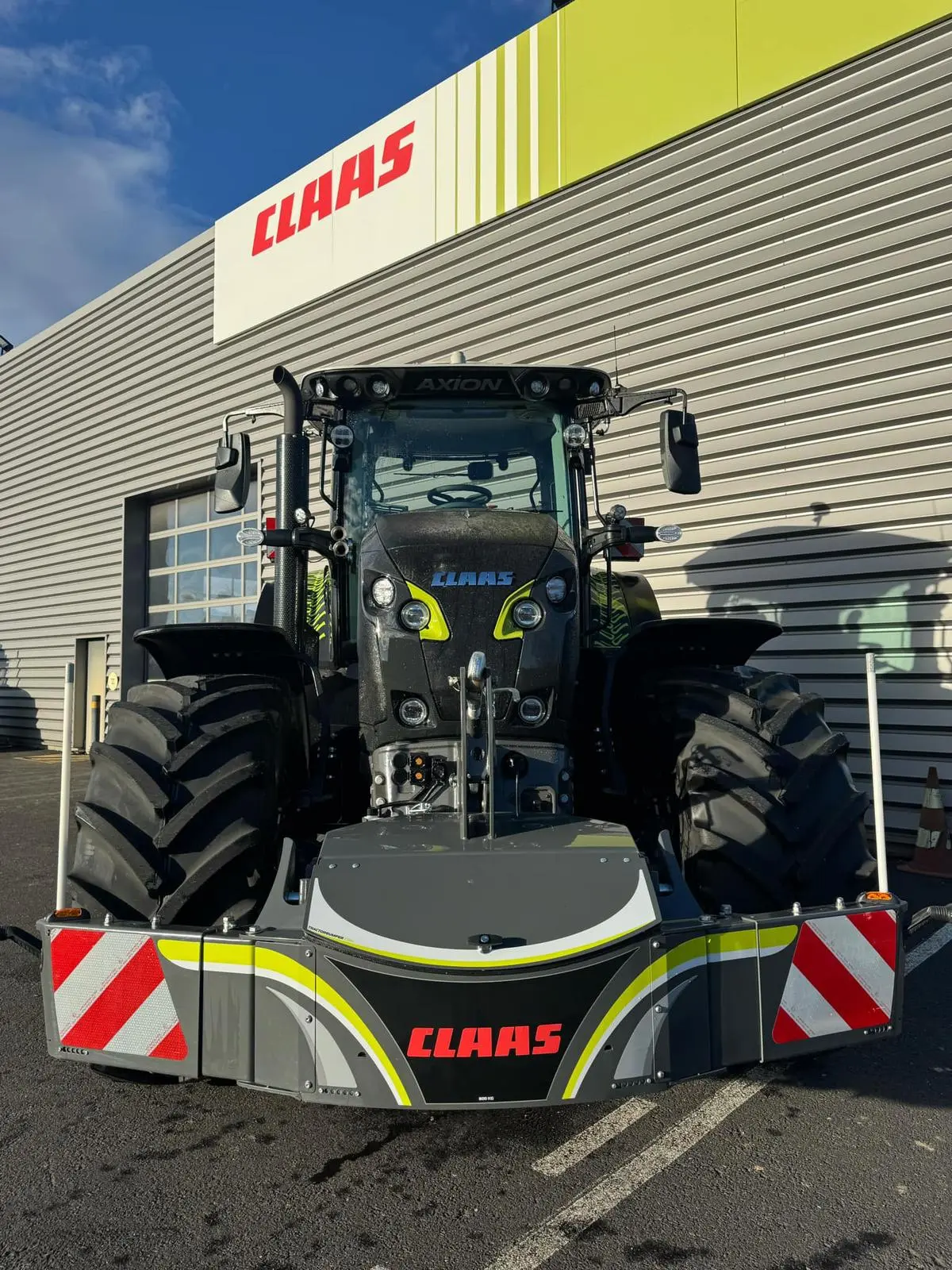 A large tractor fitted with a front weight bumper featuring red and white reflective stripes and CLAAS branding