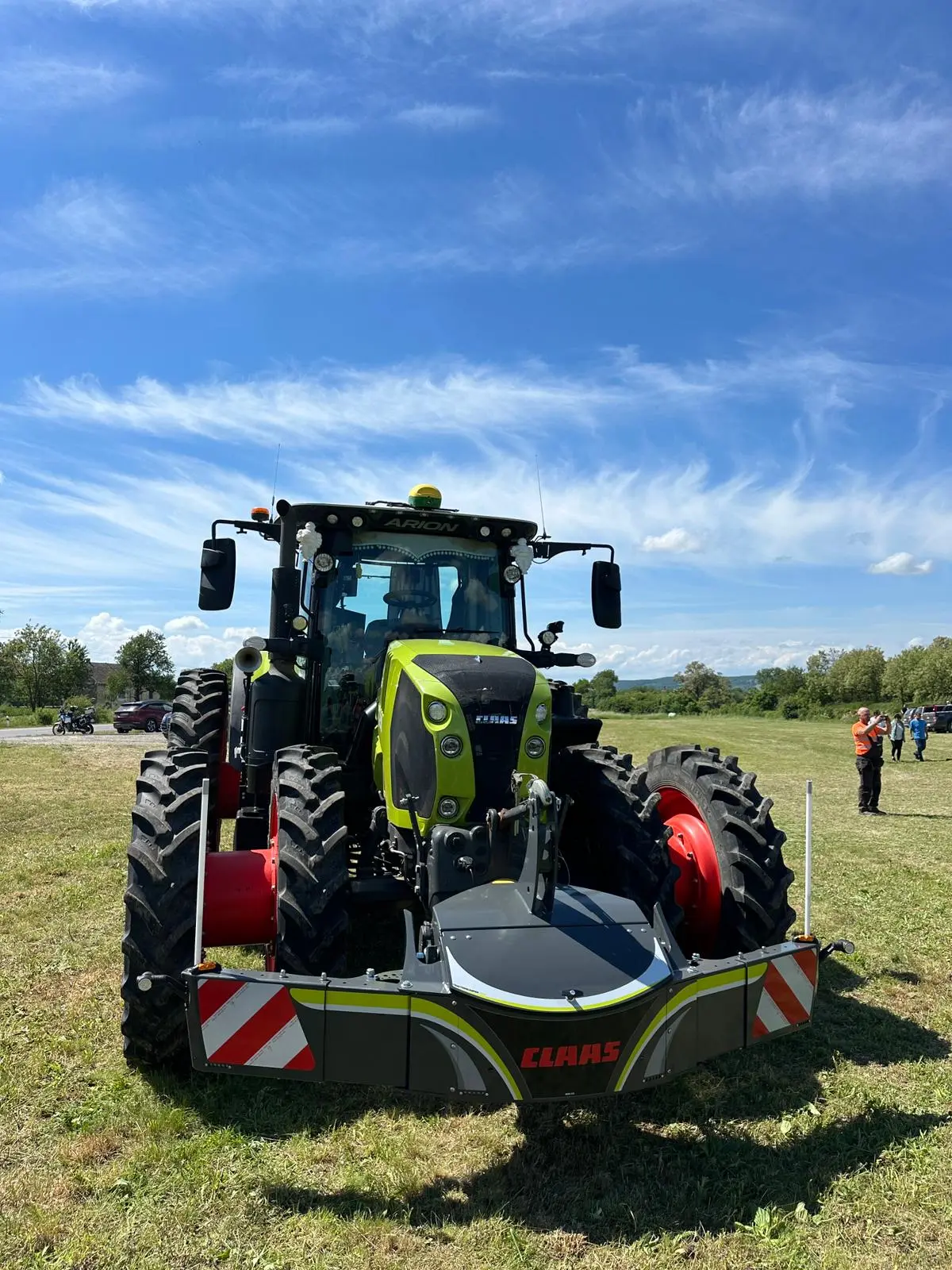 A green tractor with large tires is fitted with a front weight bumper labeled CLAAS on a grassy field