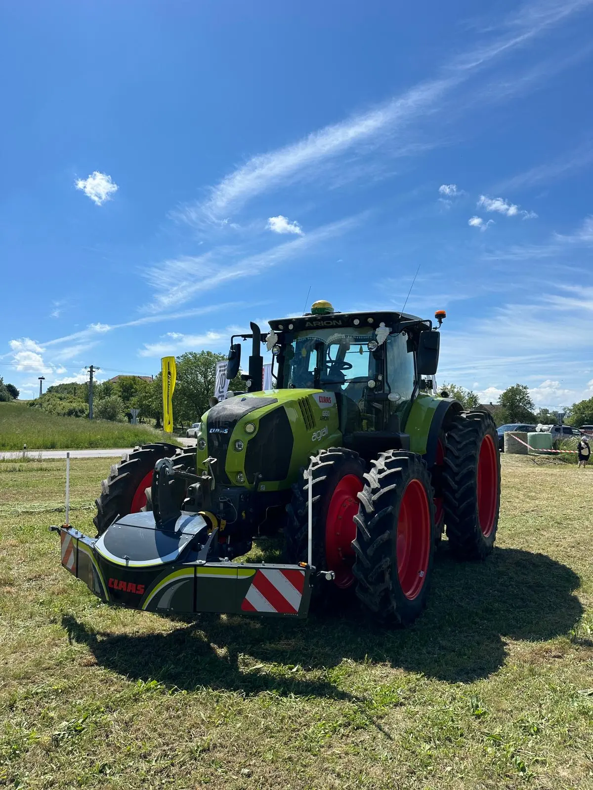 Green tractor with red wheels fitted with a front weight bumper featuring reflective stripes on grass under blue sky