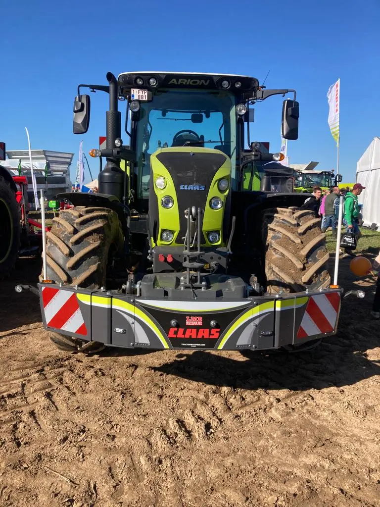 A green tractor fitted with a front weight bumper displaying CLAAS branding and red-white reflective stripes