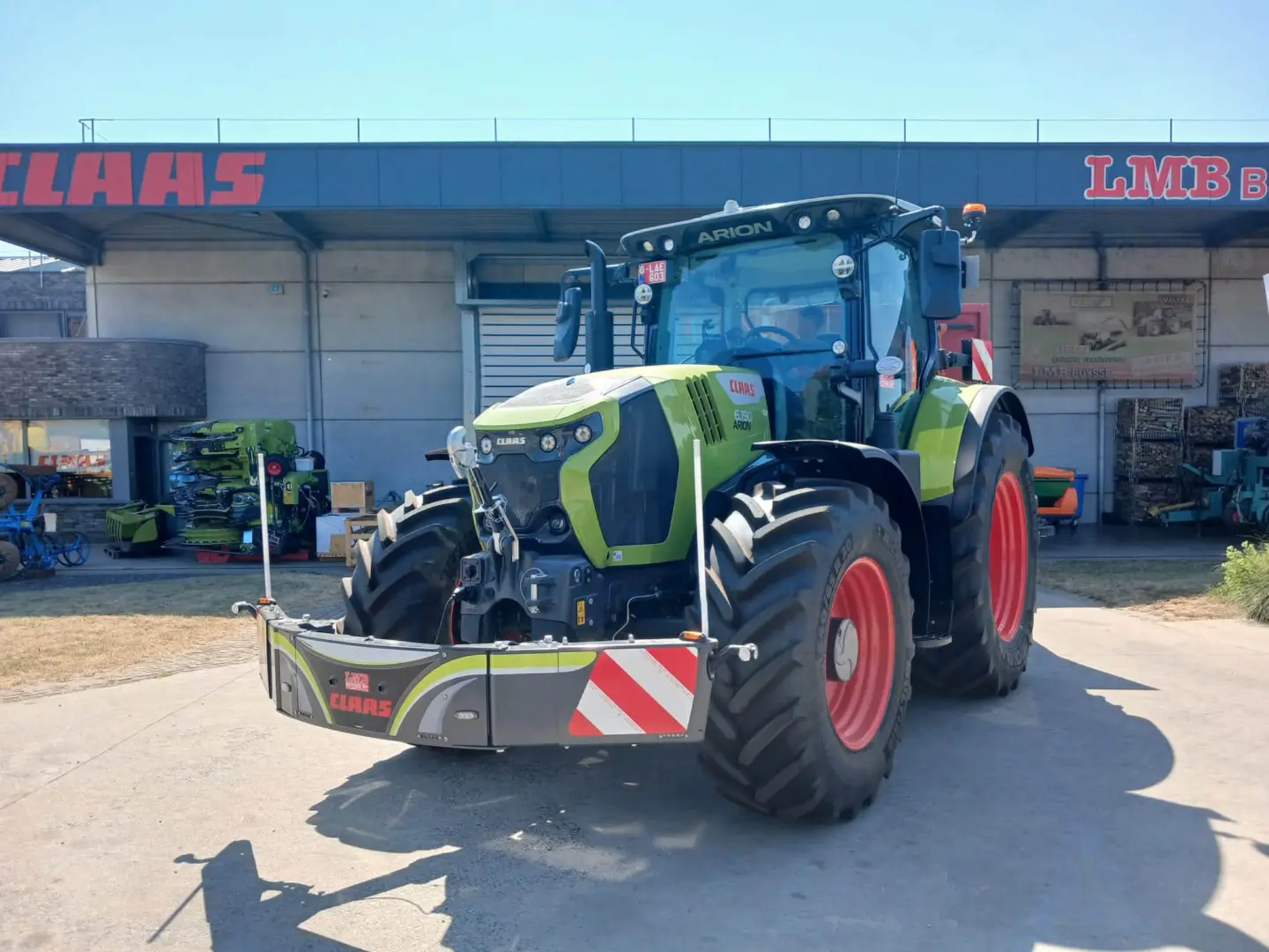 Green tractor with large front weight bumper equipped with LED lights and reflective markings in a dealership yard