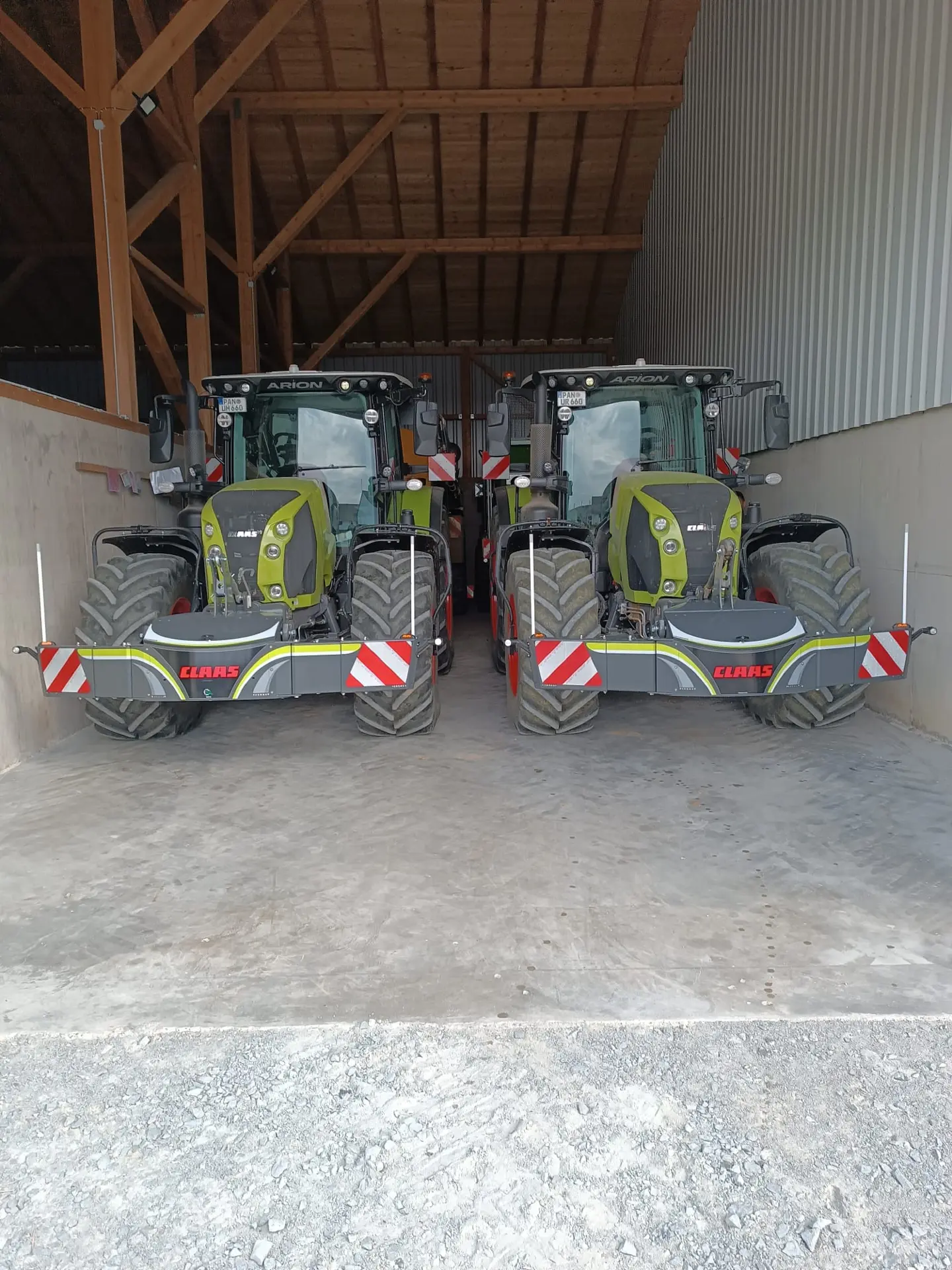 Two green tractors with front weight bumpers displaying reflective stripes parked side by side in a barn