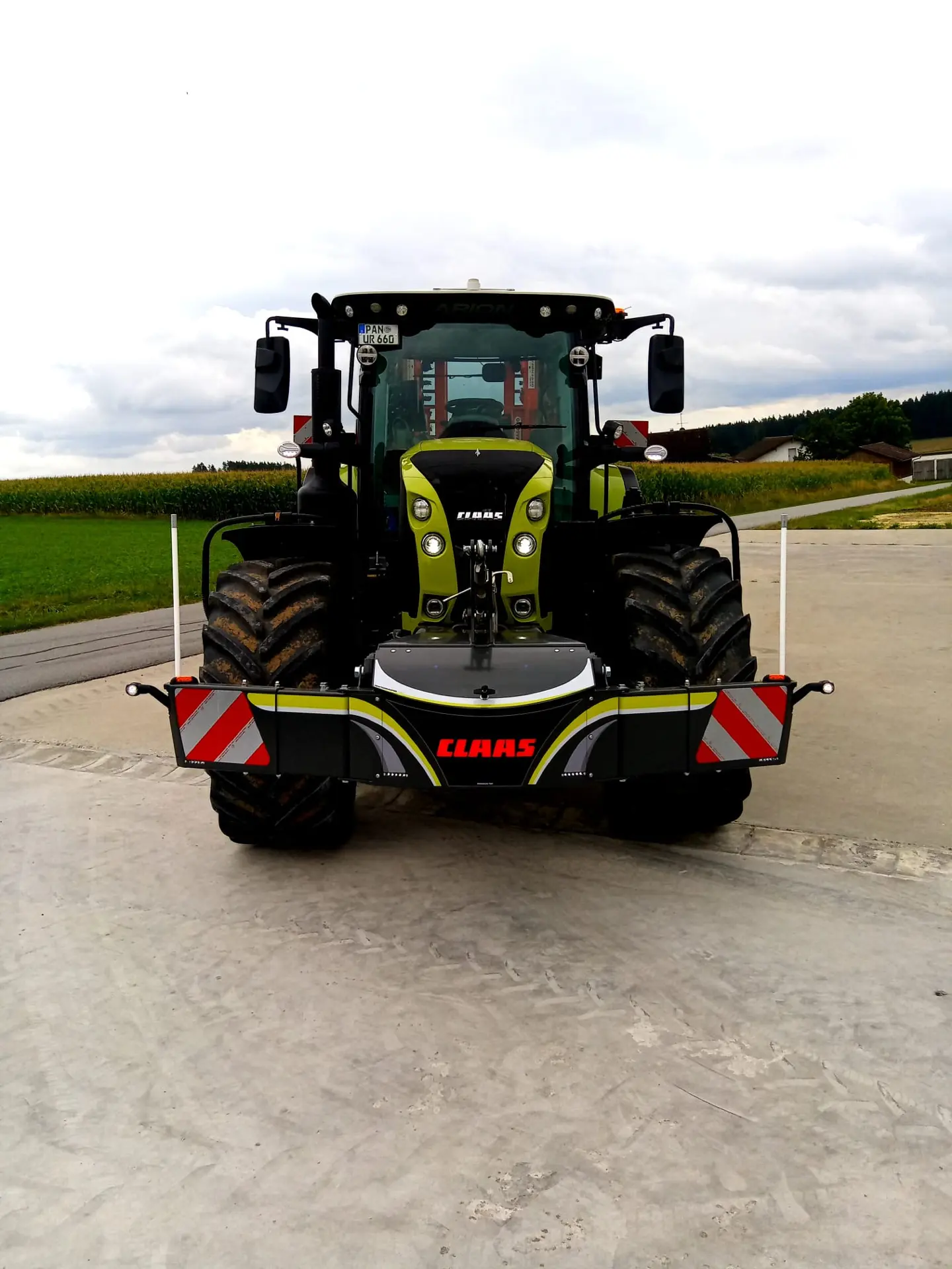 A tractor fitted with a front weight bumper featuring reflective red and white stripes and the CLAAS logo