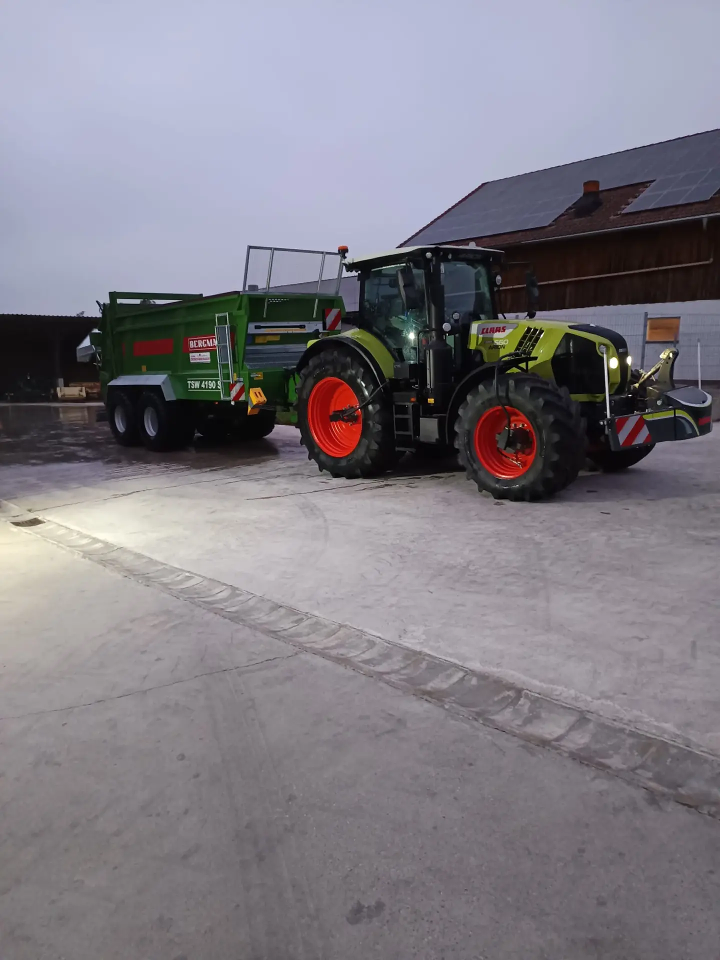 Green tractor with a front weight bumper and LED lights is parked outdoors, attached to a green trailer