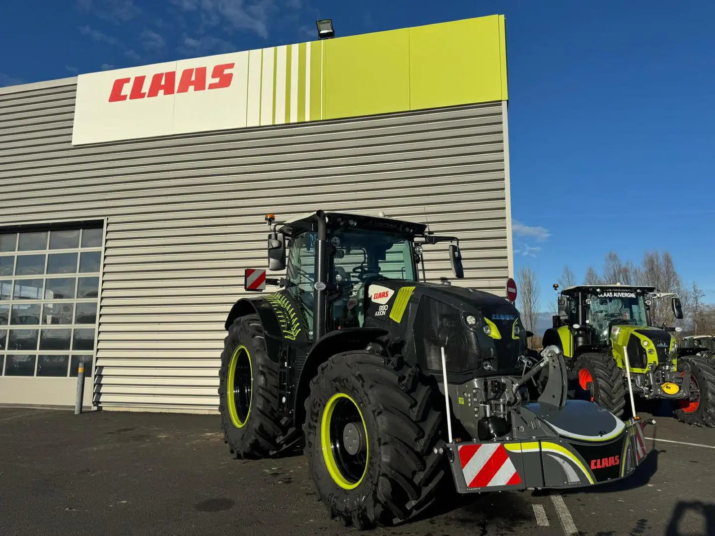 Two large tractors with yellow wheel rims and front weight bumpers are parked outside a building with a CLAAS sign