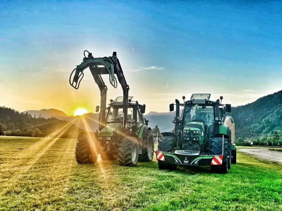Two green tractors on grass at sunset, one with a front loader and the other with a front weight bumper attached
