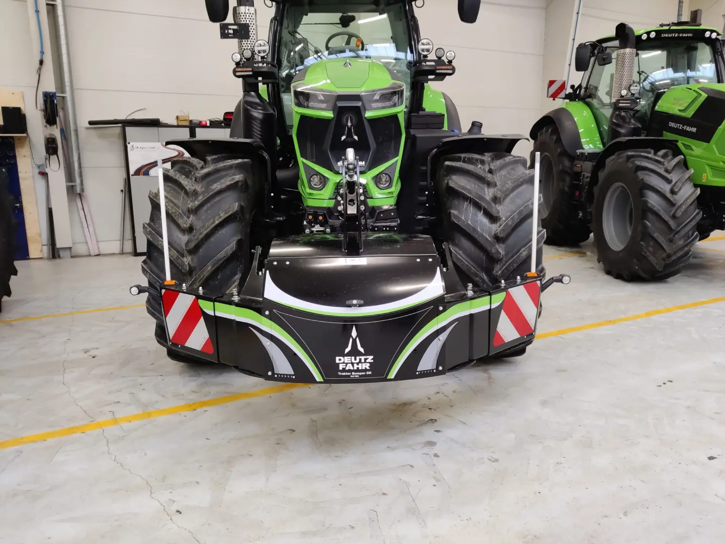 A green tractor with a Deutz-Fahr branded front weight bumper and reflective safety markings in an indoor garage