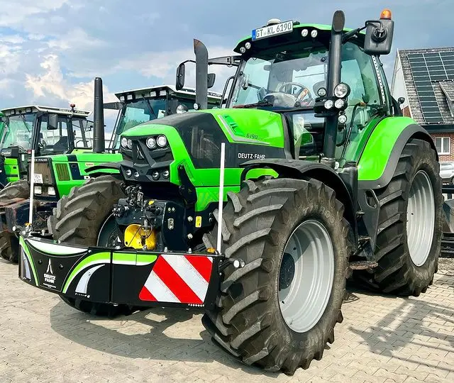 A green tractor fitted with a front weight bumper featuring red and white reflective stripes on a paved lot
