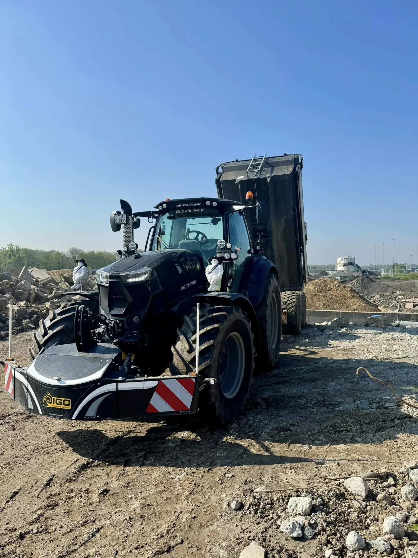 A tractor with a front weight bumper and striped reflectors is parked on a construction site near a dump truck