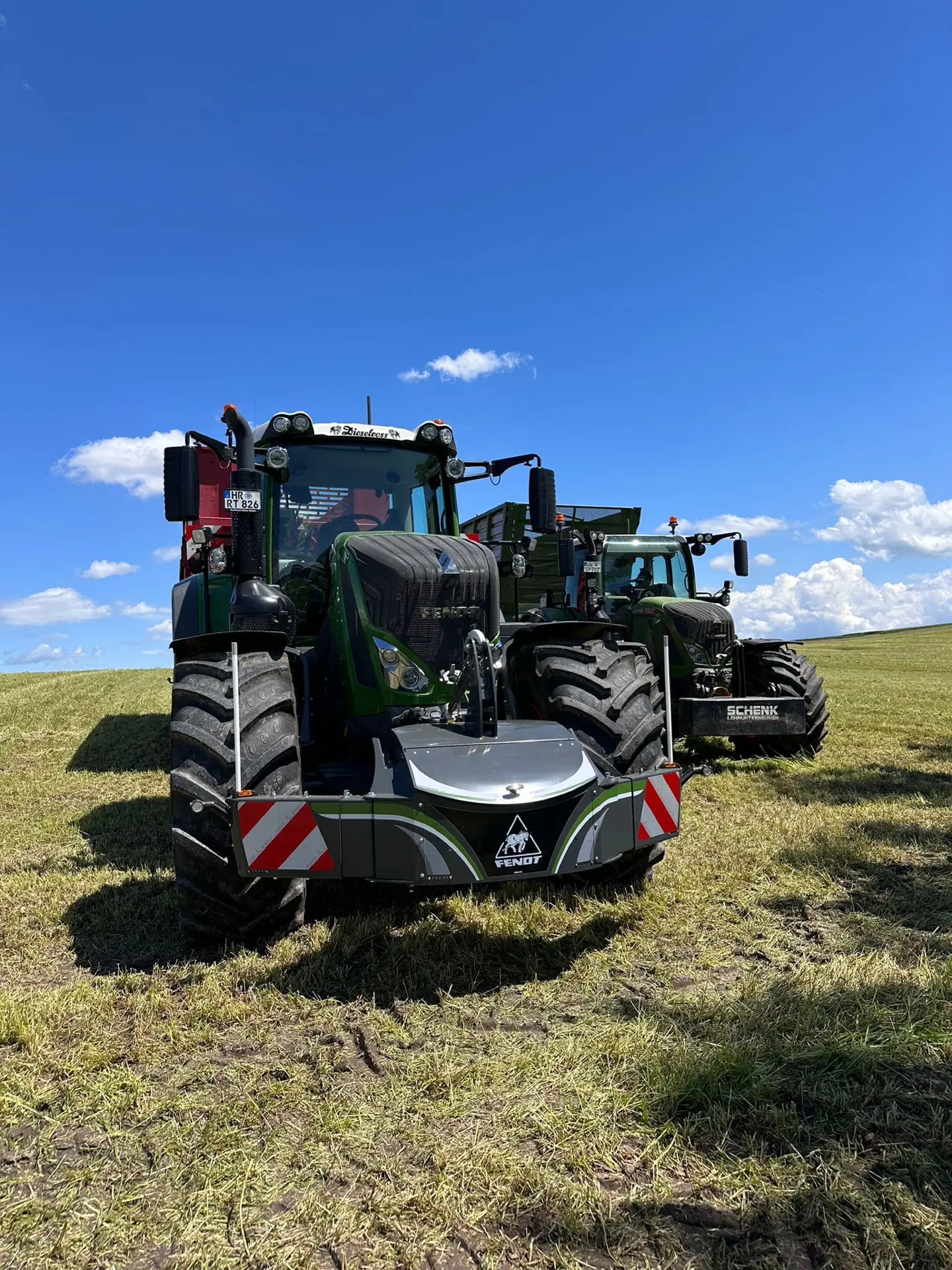Two green tractors parked on grass, each equipped with a front weight bumper marked with reflective red stripes