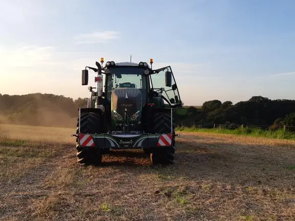 A tractor in a field with a front weight bumper attached, photographed from the front at sunset