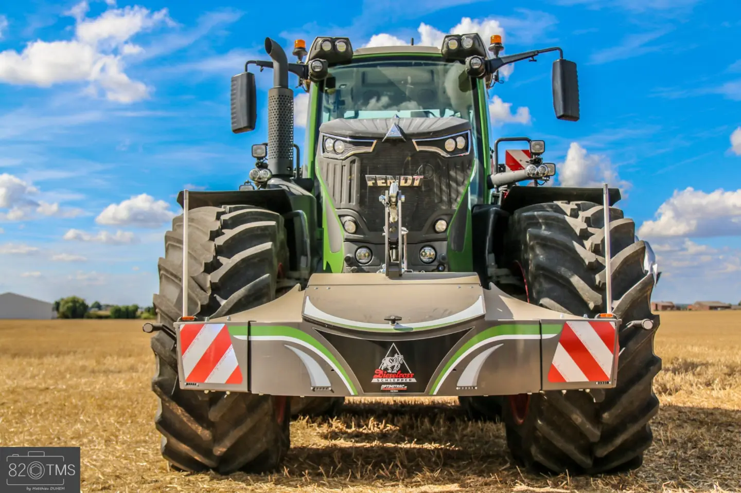 A green tractor with a large front weight bumper featuring red and white warning stripes on a field