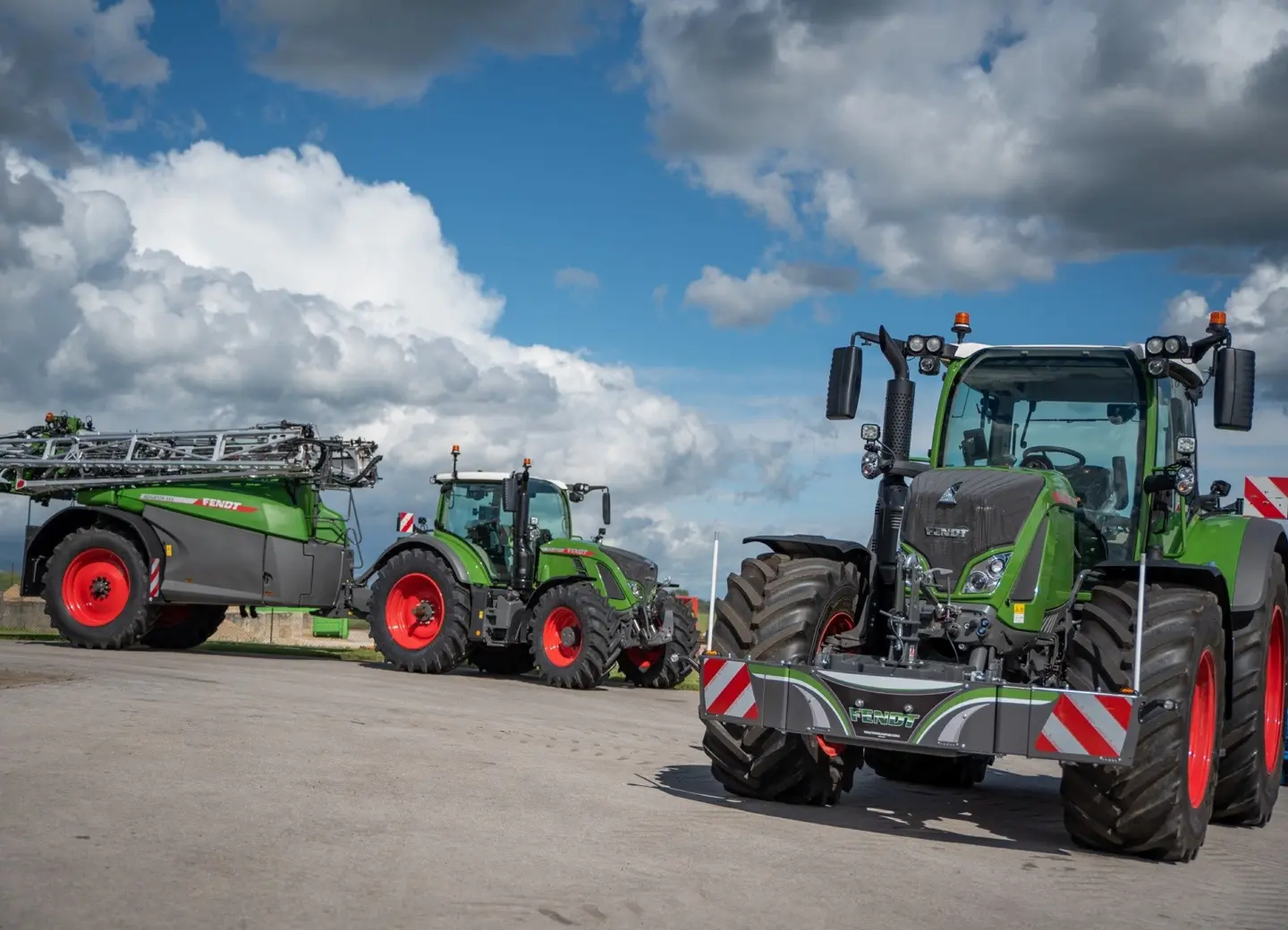 Two green tractors with red wheels are parked outside, both fitted with silver front weight bumpers with reflective stripes