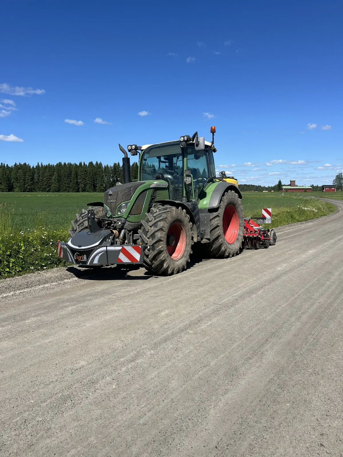 Green tractor with a front weight bumper and rear implement parked on a country road by a field under blue sky