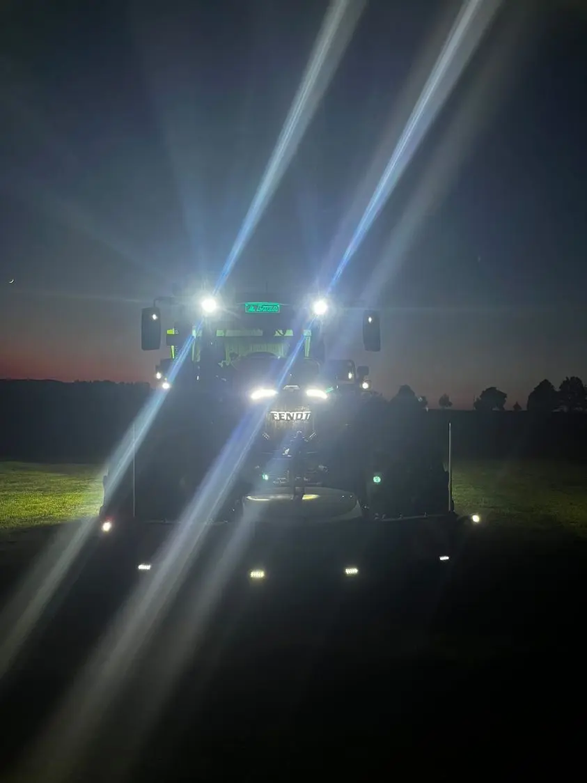 Tractor with headlights on in the dark, fitted with a front weight bumper on a grassy field