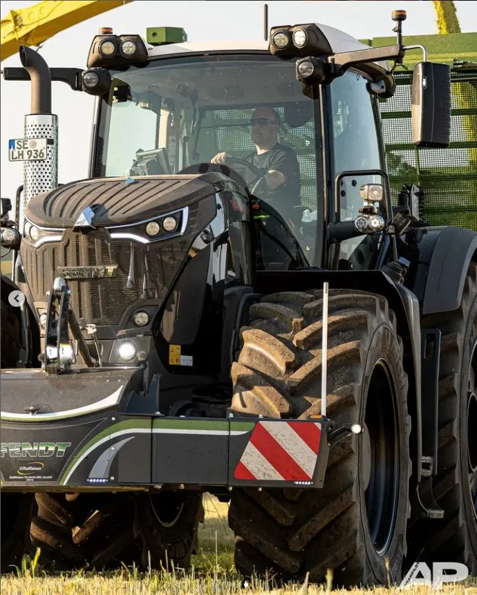A large tractor with a front weight bumper featuring red and white reflective stripes on a grassy field