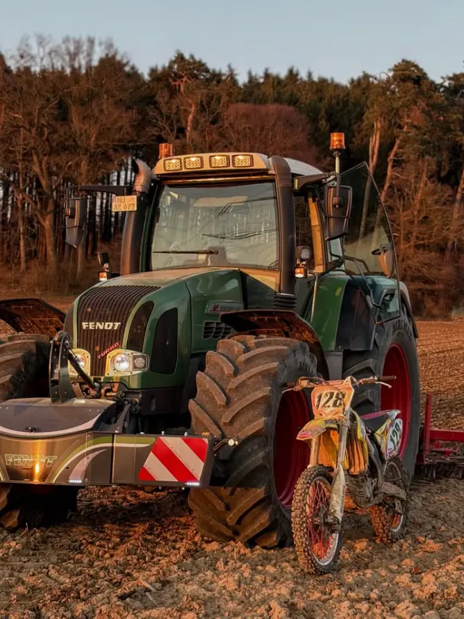 Green tractor with a front weight bumper attached, parked in a field beside a dirt bike with number 126