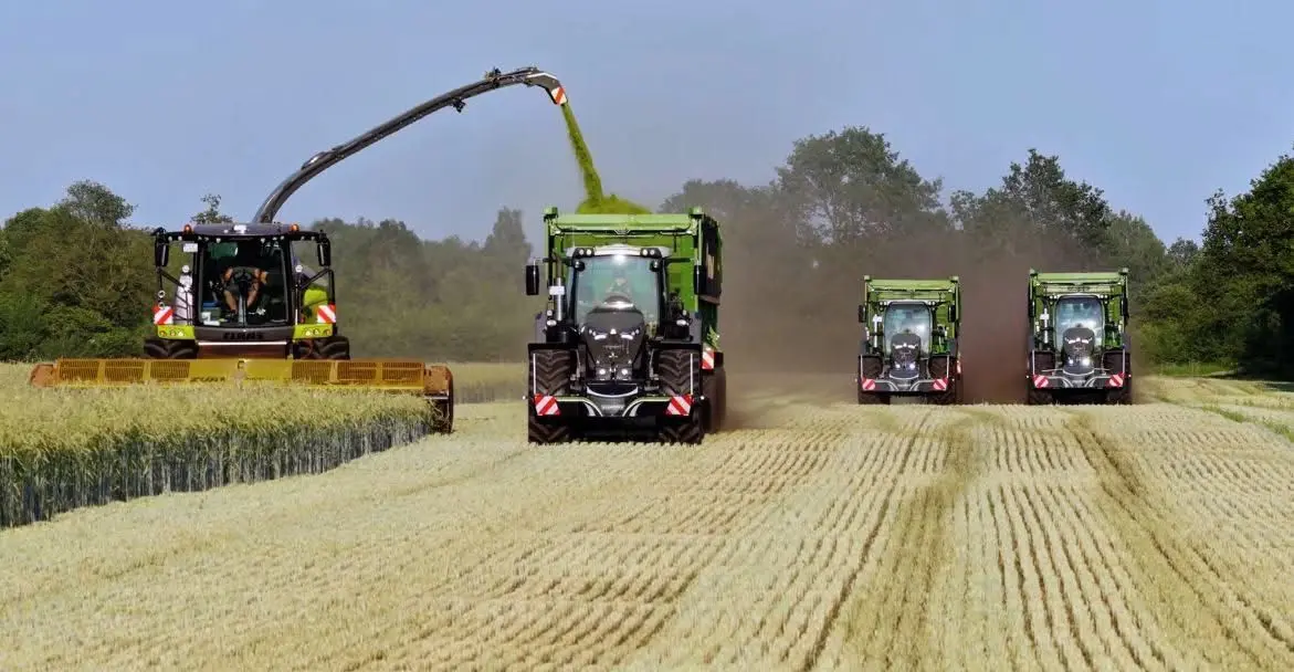 Four green agricultural machines with front weight bumpers working in a harvested field on a sunny day