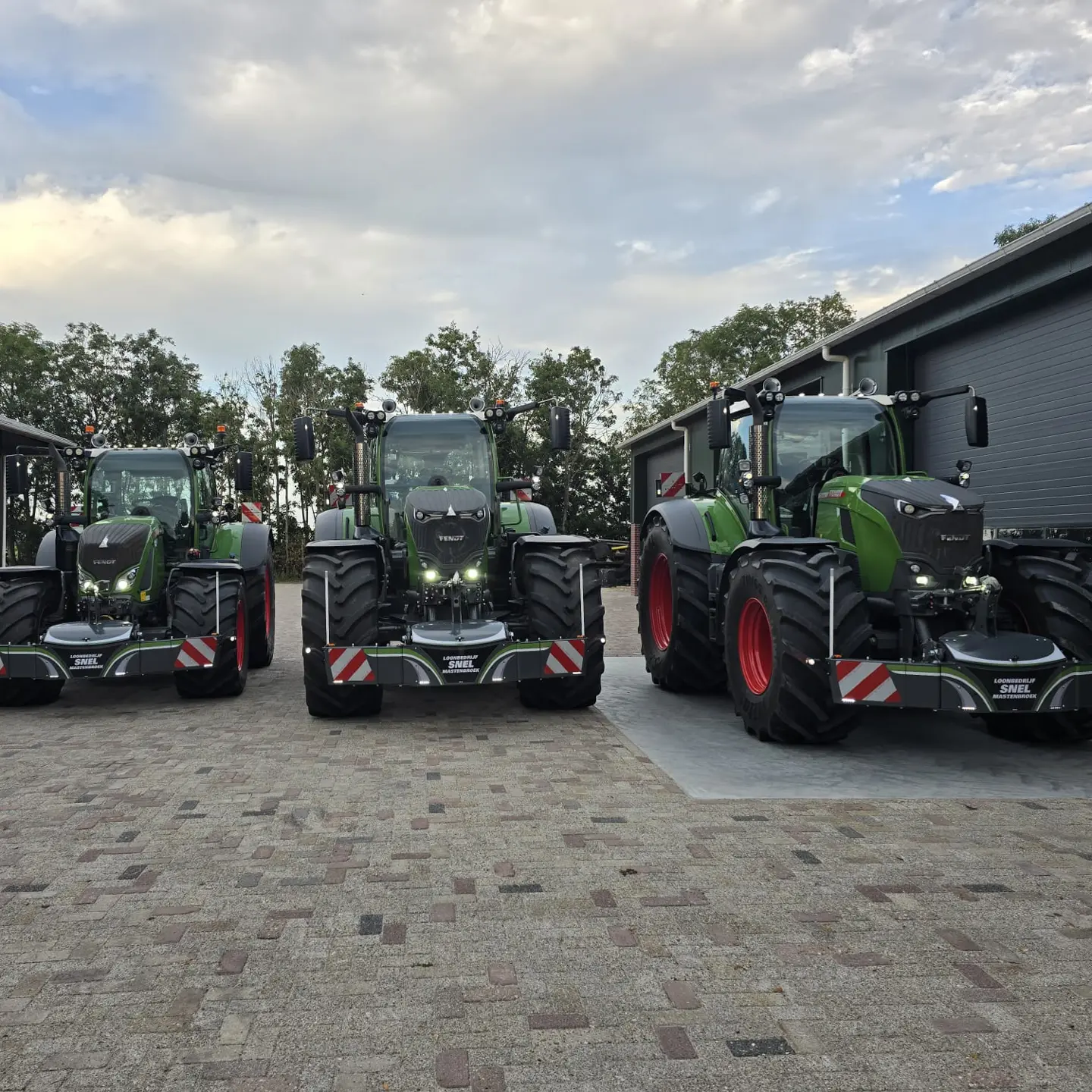 Three green tractors with large front weight bumpers are parked side by side on a paved lot near a building