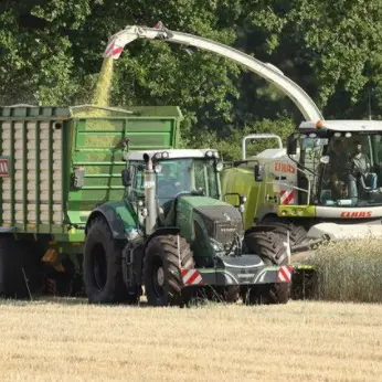 A tractor with a front weight bumper pulls a trailer being filled with chopped crop from a forage harvester in a field
