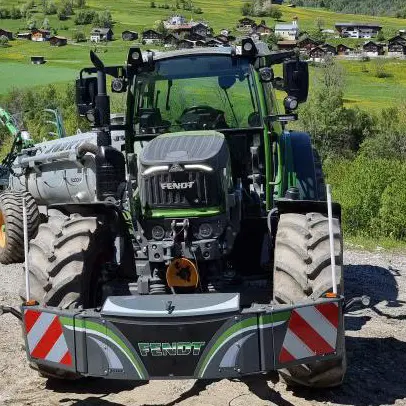 A tractor with large front weight bumper marked Fendt and red-white reflectors parked on a rural gravel road