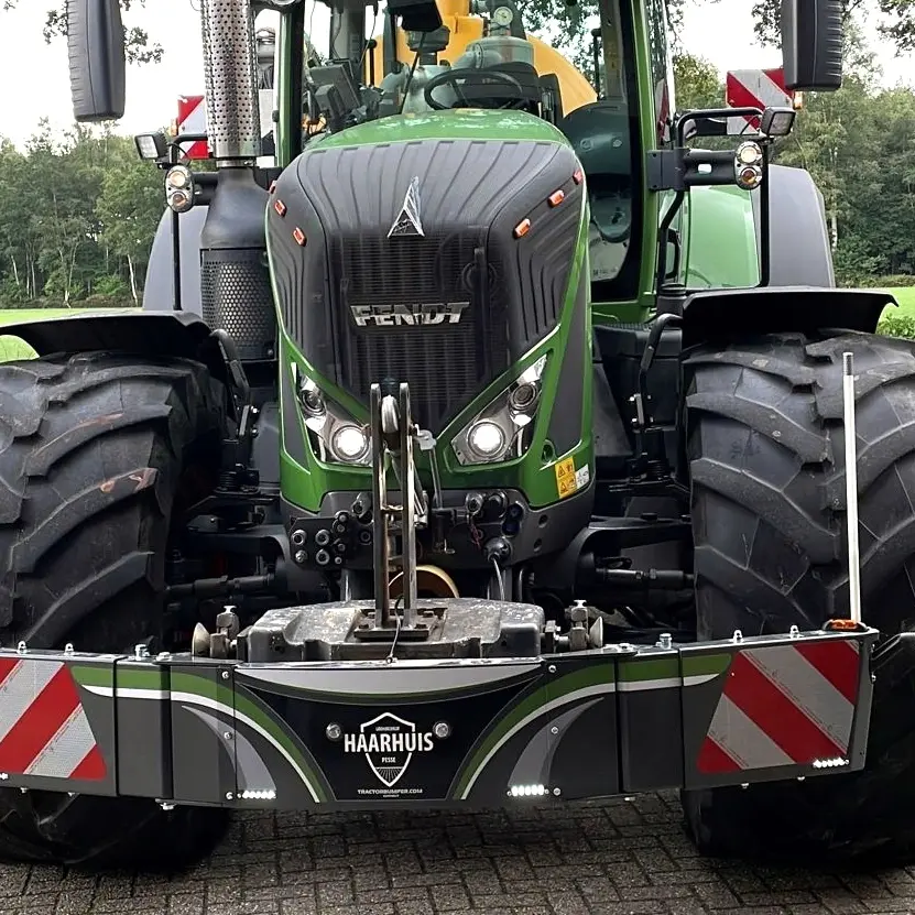 A green tractor with large tires fitted with a front weight bumper displaying red and white safety stripes