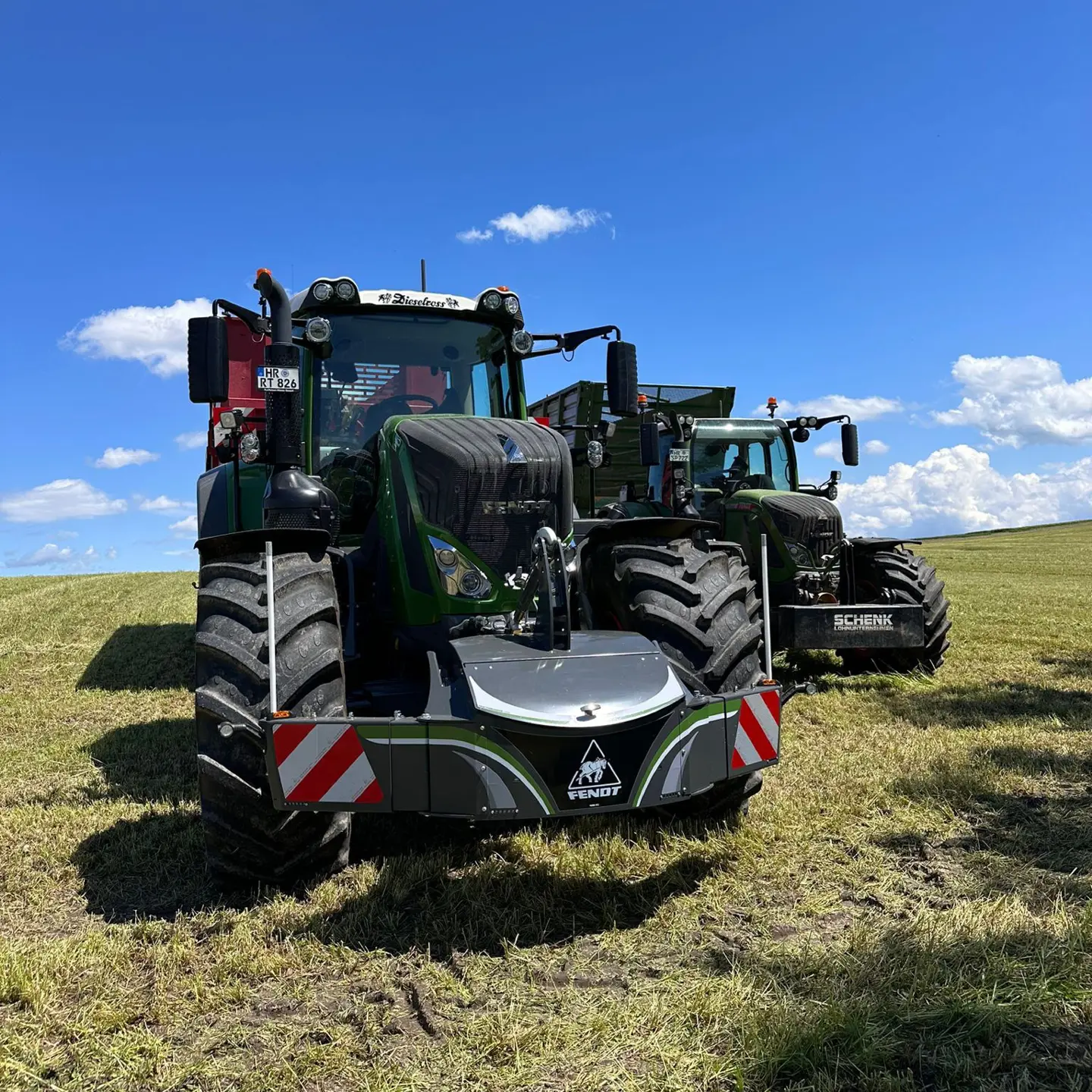 Two green tractors on a grassy field, each fitted with large front weight bumpers and red and white safety markings