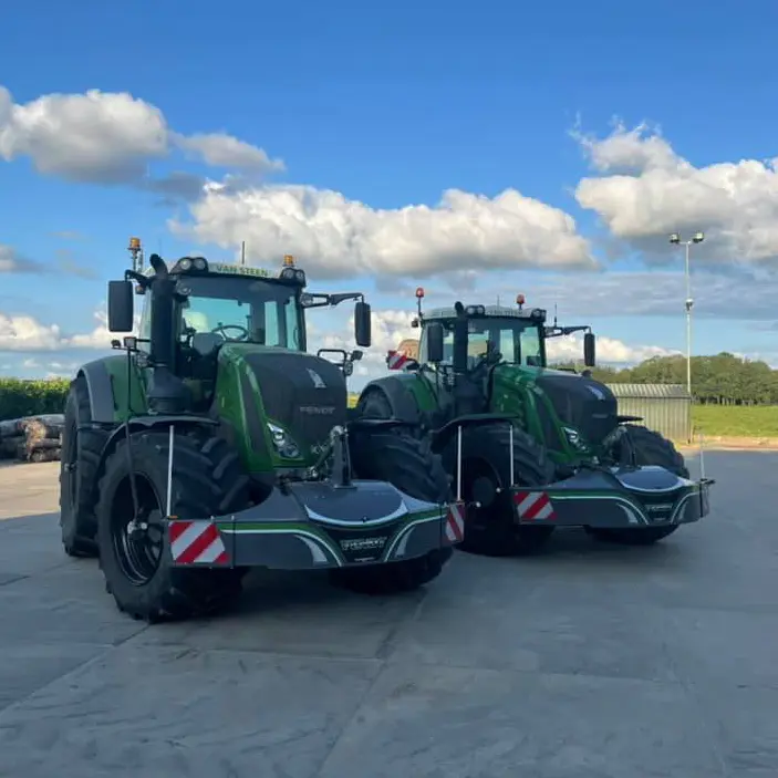 Deux tracteurs verts sont stationnés sur du béton, chacun équipé d'un grand pare-poids avant avec marquages de sécurité
