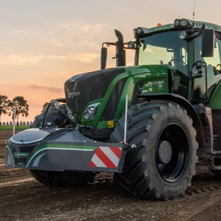 Tracteur vert avec un grand pare-poids avant fixé, garé dans un champ au coucher du soleil