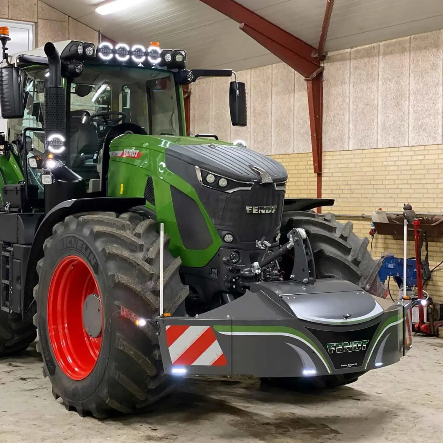 Tracteur vert avec un grand pare-chocs avant lesté avec bandes réfléchissantes rouges et blanches dans un garage intérieur