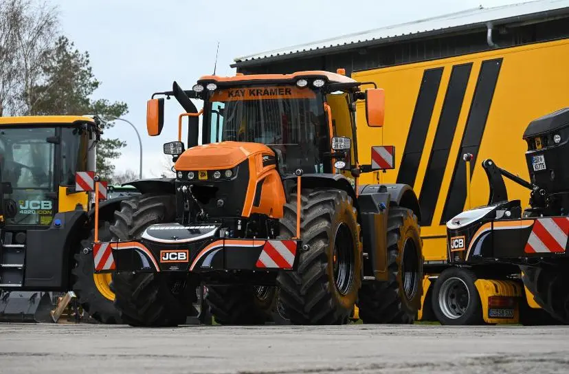 Orange tractor with a front weight bumper labeled JCB, parked outdoors beside other machinery and equipment
