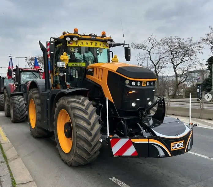 A JCB tractor with a front weight bumper featuring LED lights and reflective safety markings on a road.