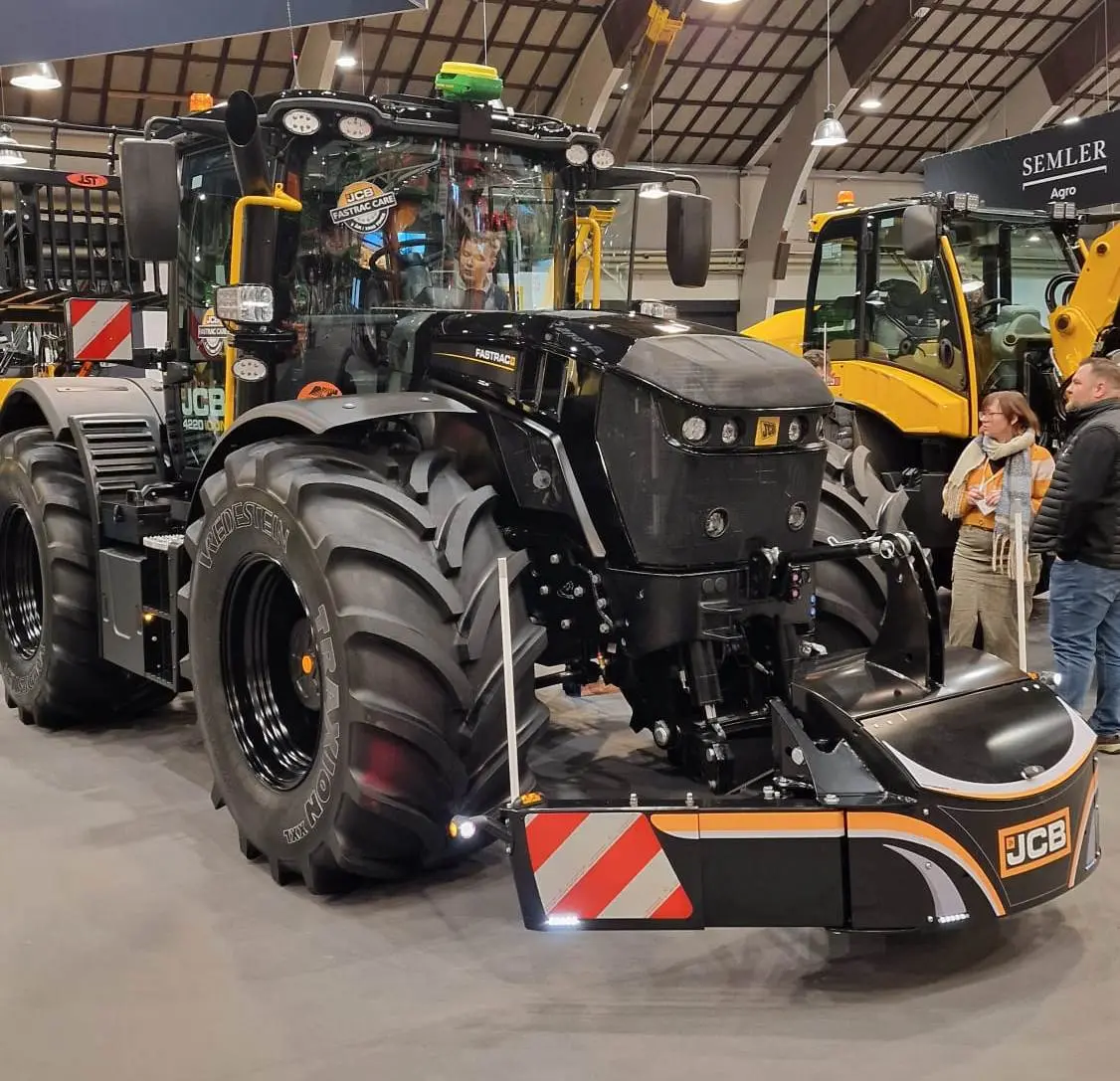 Large black tractor with a front weight bumper featuring red and white safety decals and a JCB logo on display indoors