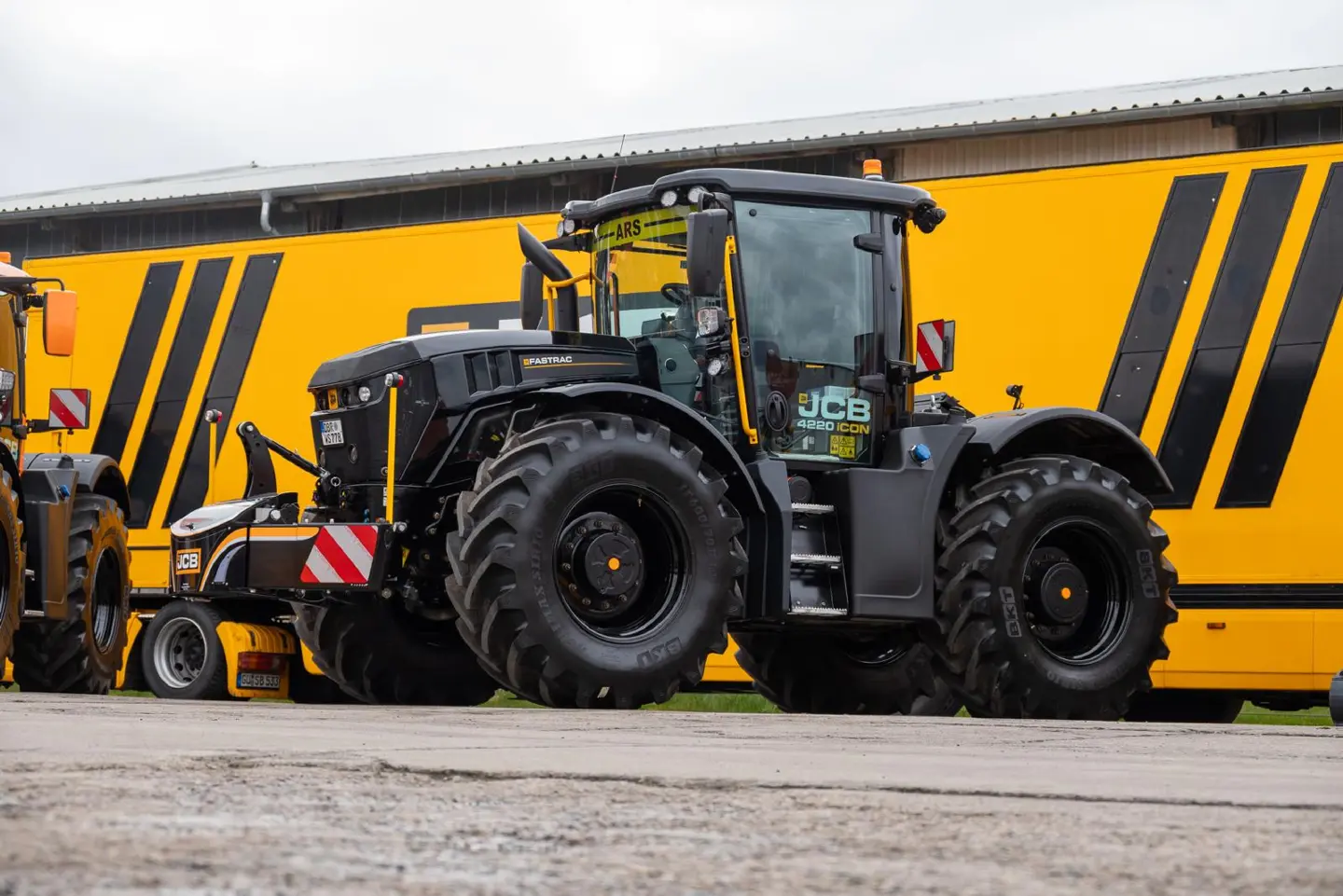 A large black tractor with a front weight bumper attachment parked in front of a yellow vehicle