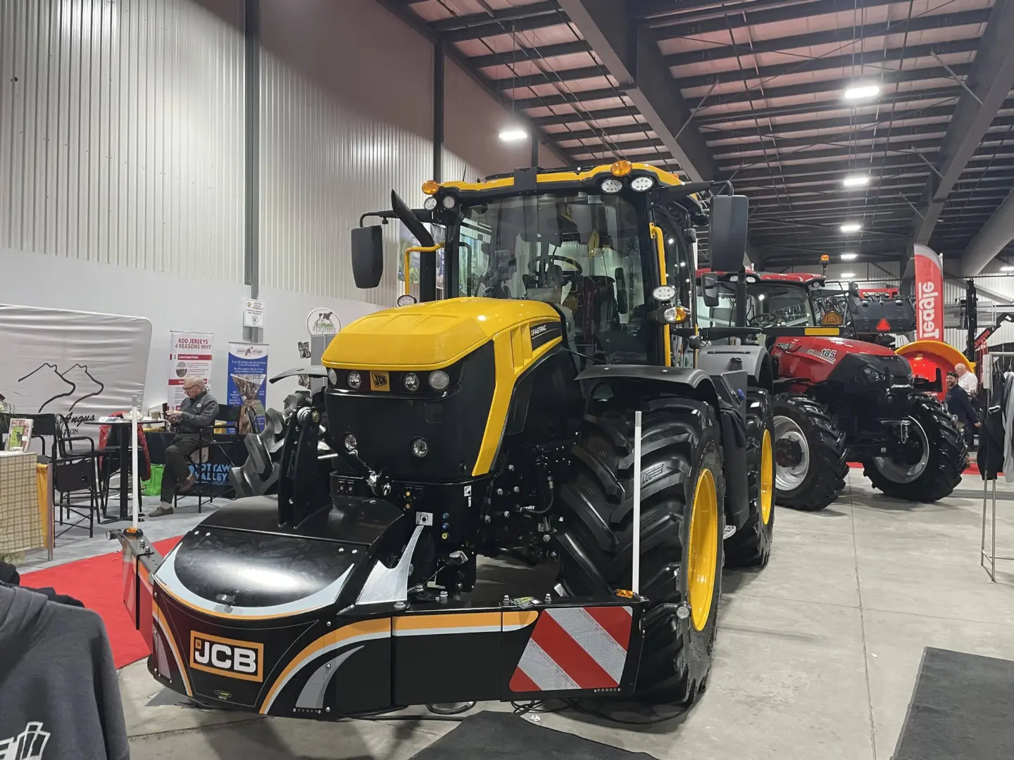 A yellow and black tractor fitted with a JCB front weight bumper is displayed indoors at an exhibition.