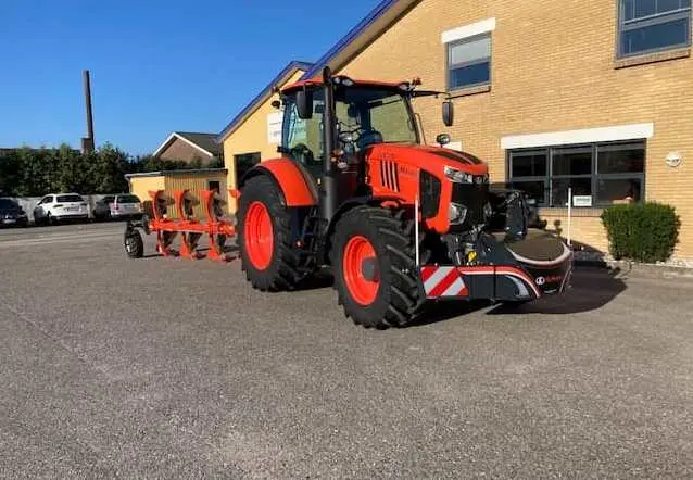 An orange tractor fitted with a front weight bumper is parked on pavement, attached to a large agricultural implement
