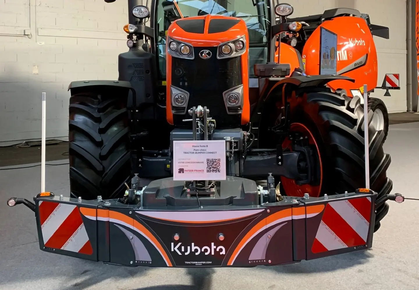 Orange tractor with a front weight bumper featuring Kubota branding and red-white safety stripes indoors