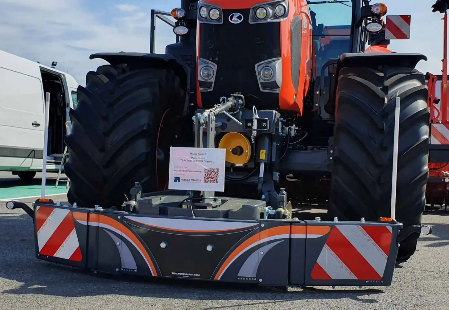 Large orange tractor with a mounted front weight bumper featuring reflective red and white diagonal stripes