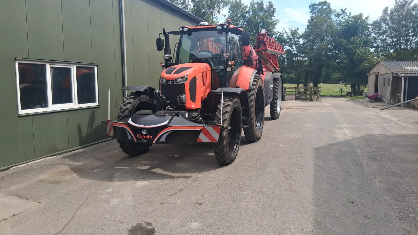 Orange tractor with a large front weight bumper featuring red and white reflective stripes on a farm driveway