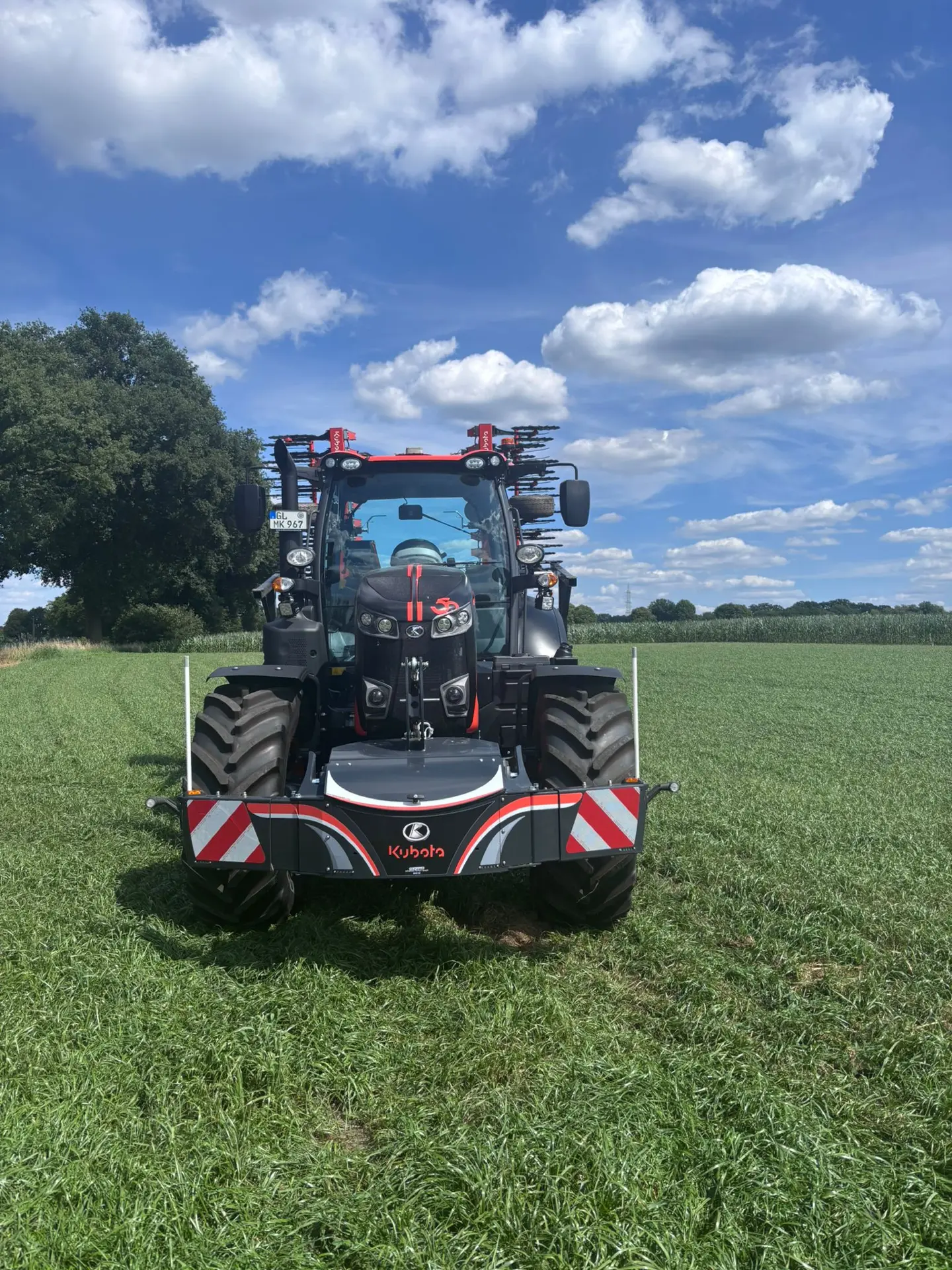Tractor with a Kubota front weight bumper featuring red and white safety stripes parked on grass under a blue sky