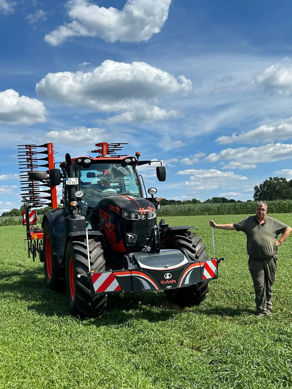 A man stands next to a Kubota tractor in a field, featuring a large front weight bumper with red and white stripes