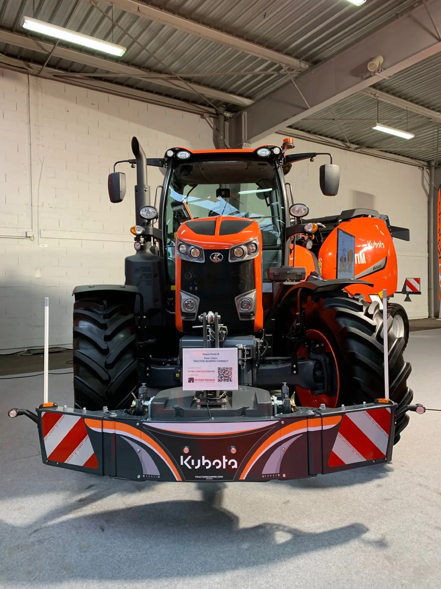 Front view of an orange tractor indoors with a Kubota-branded front weight bumper attached.